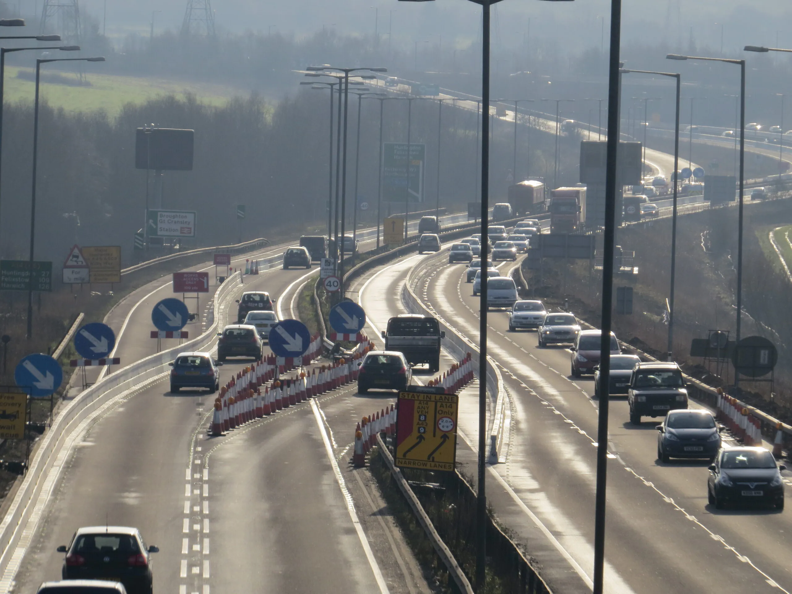 Highway construction zone with traffic cones, barriers, and vehicles navigating through reduced lanes.
