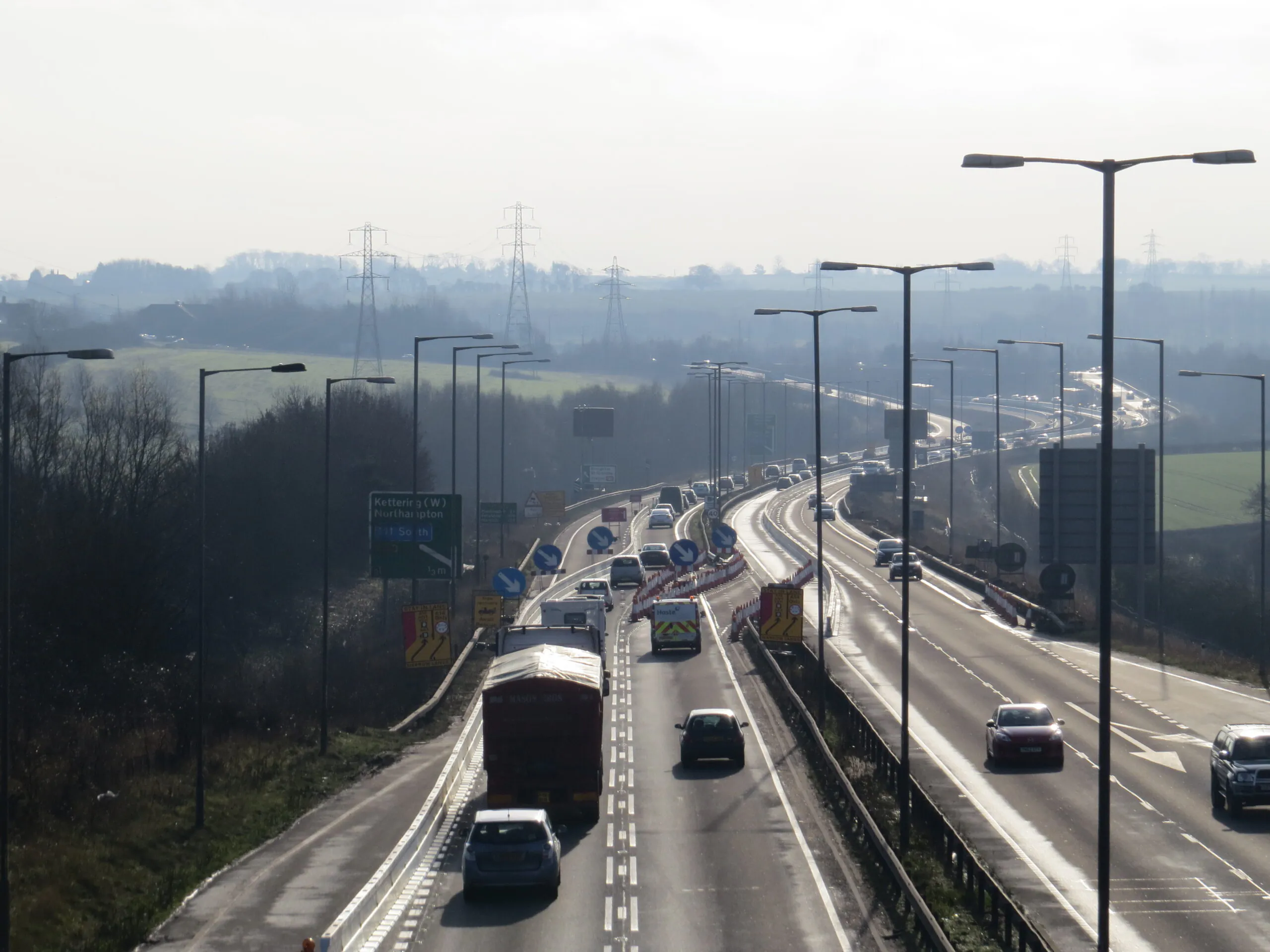Busy highway with multiple lanes of traffic, roadwork signs, and barriers indicating ongoing construction or maintenance.