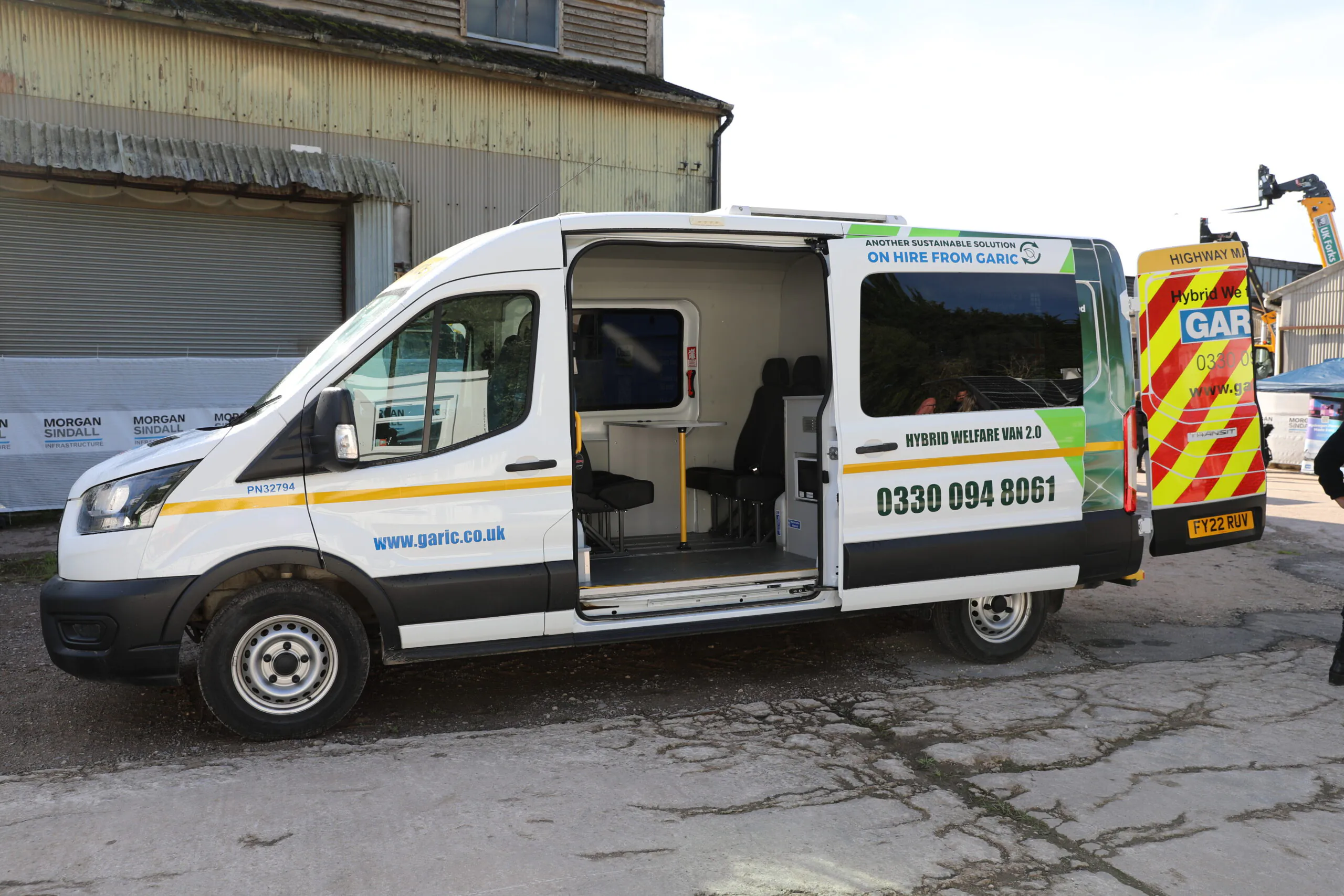 White van labeled "garic.co.uk" with green and yellow stripes, side door open revealing interior seating and contact details.