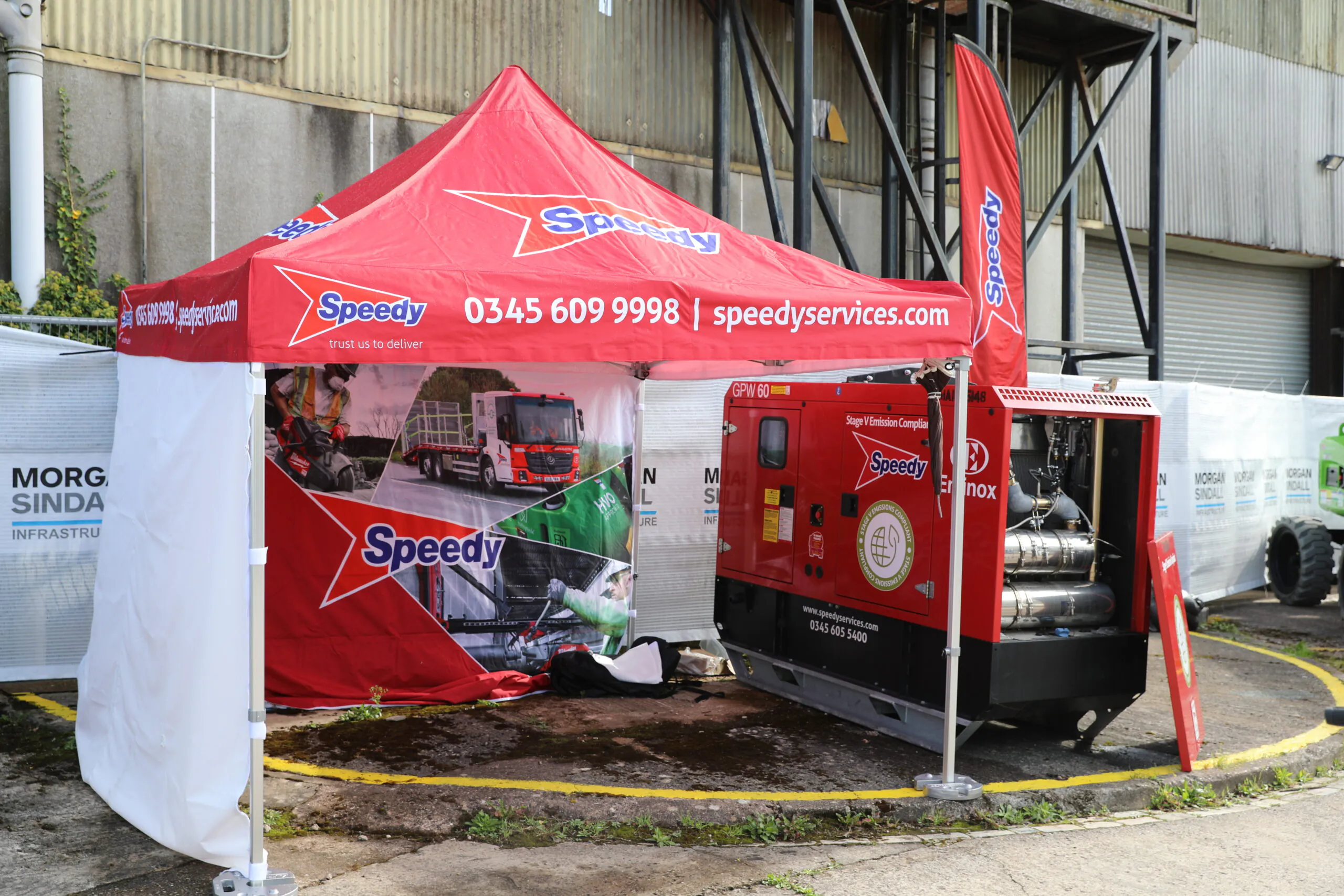 Red "Speedy Services" tent displaying contact information and service images, with equipment placed underneath.