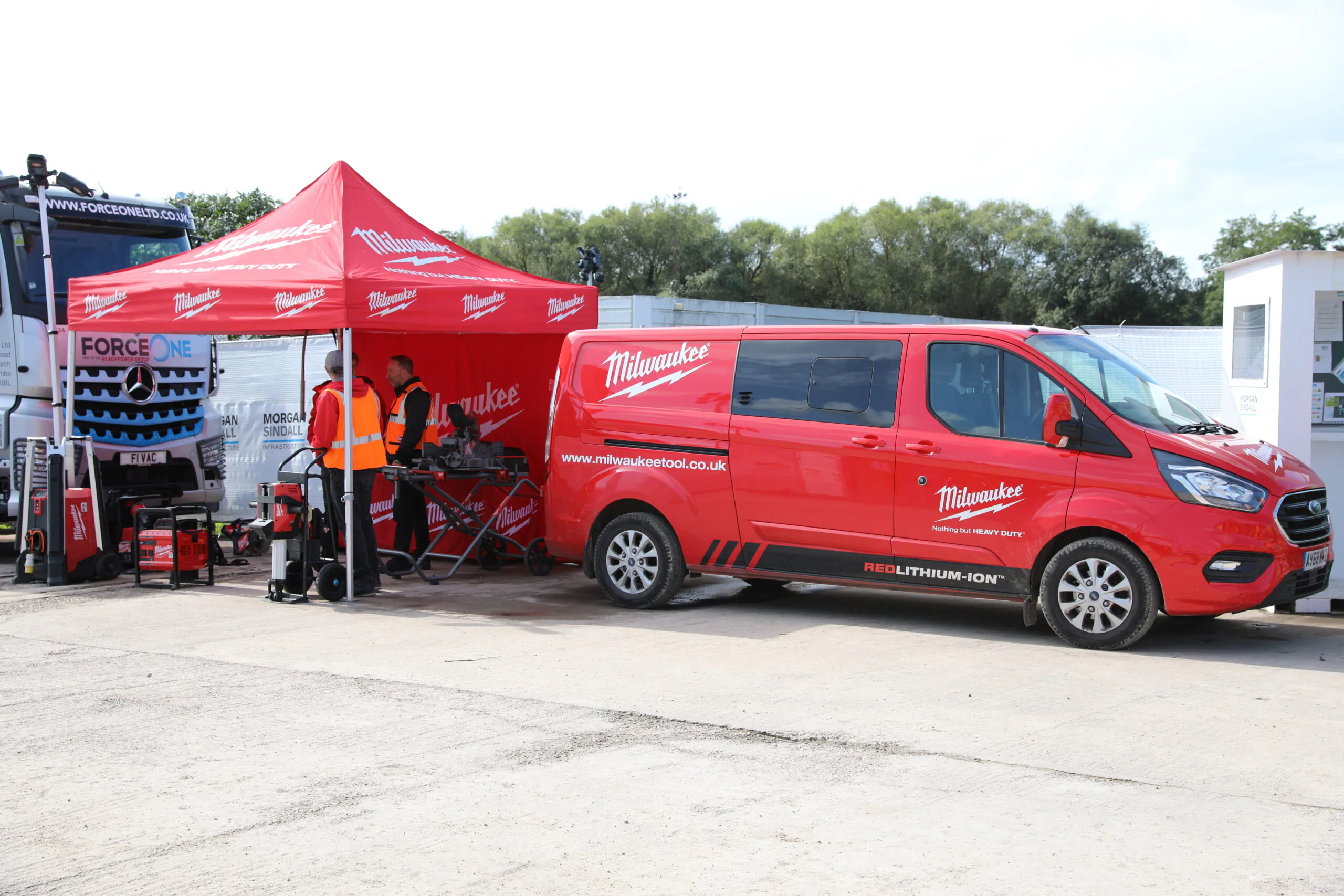 Red Milwaukee Tool van parked beside a red tent displaying tools for demonstration or sale.