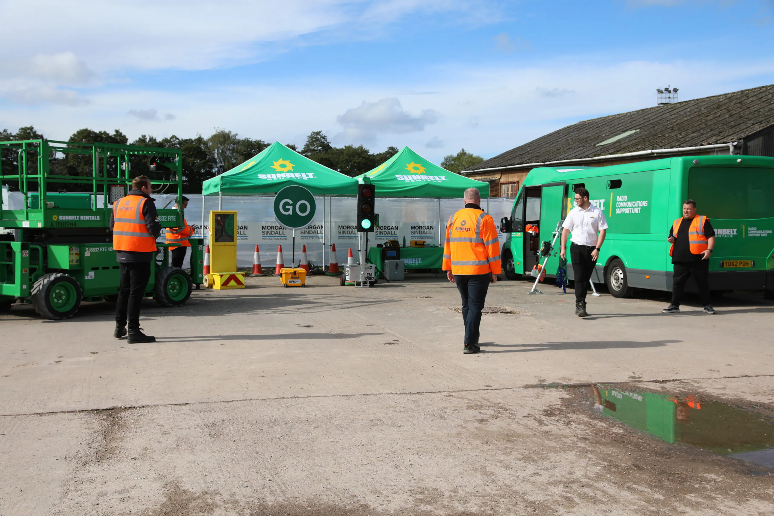 Expanded view of the Sunbelt Rentals construction site setup with tents, van, and workers in high-visibility vests walking around.