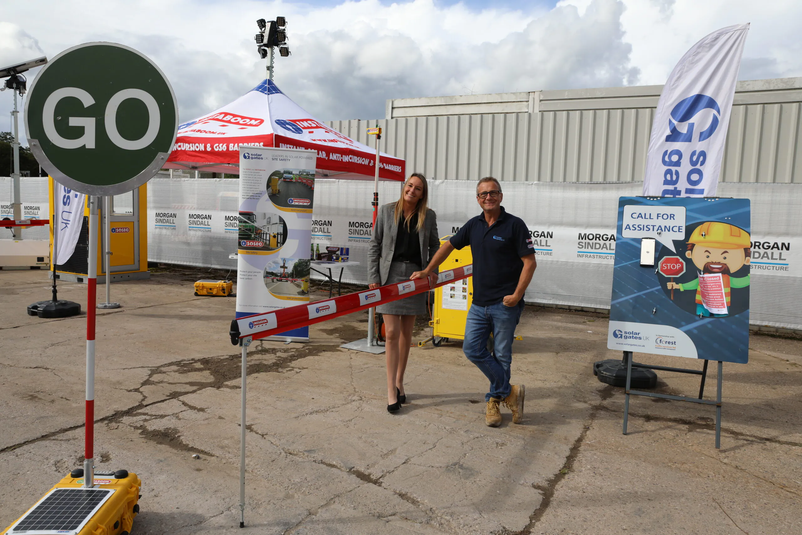 Two people standing side-by-side holding scissors, appearing ready to cut a ribbon at an event.