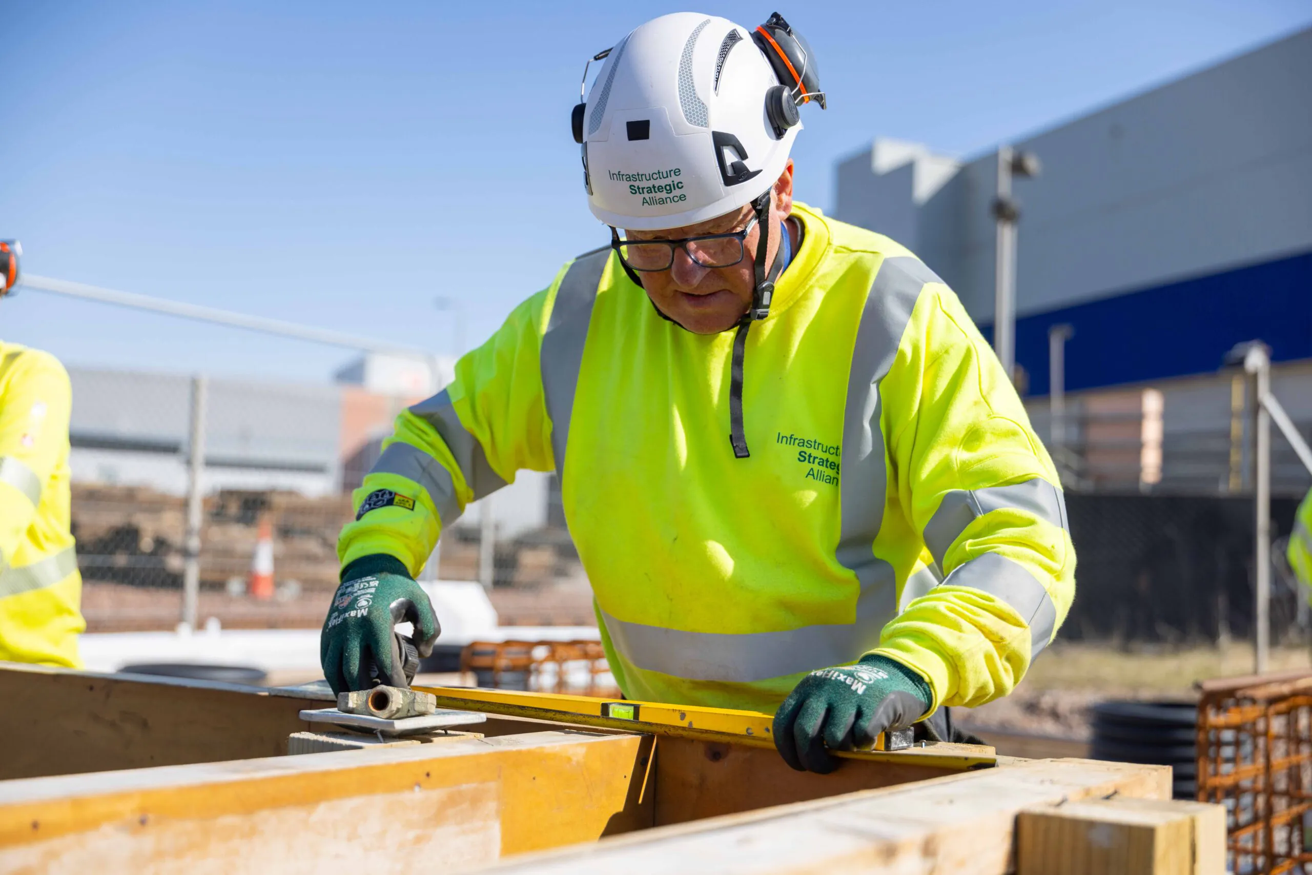 Worker in high-visibility clothing reinforces steel bars for concrete pouring at an outdoor construction site.