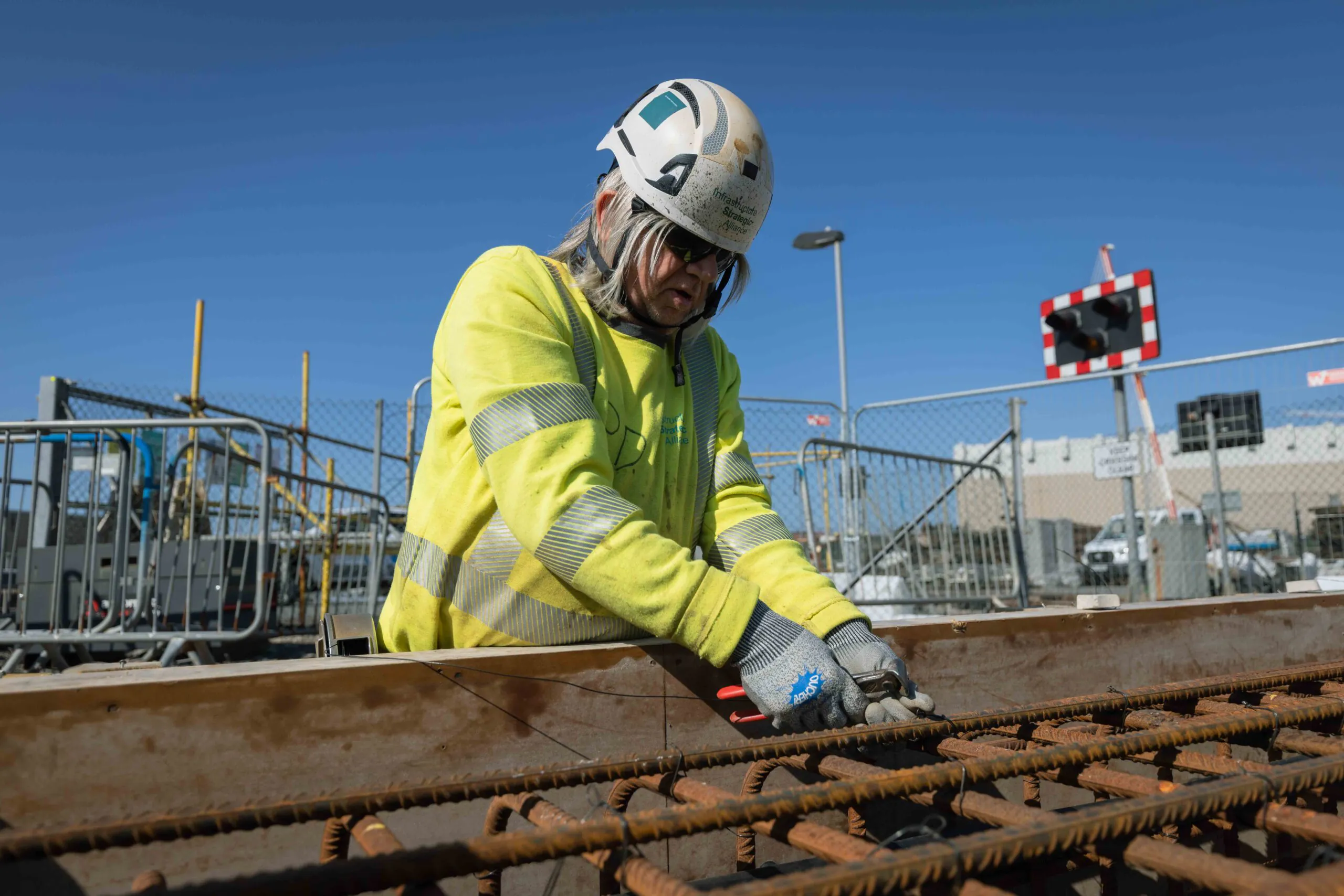 Worker in high-visibility clothing reinforces steel bars for concrete pouring at an outdoor construction site.
