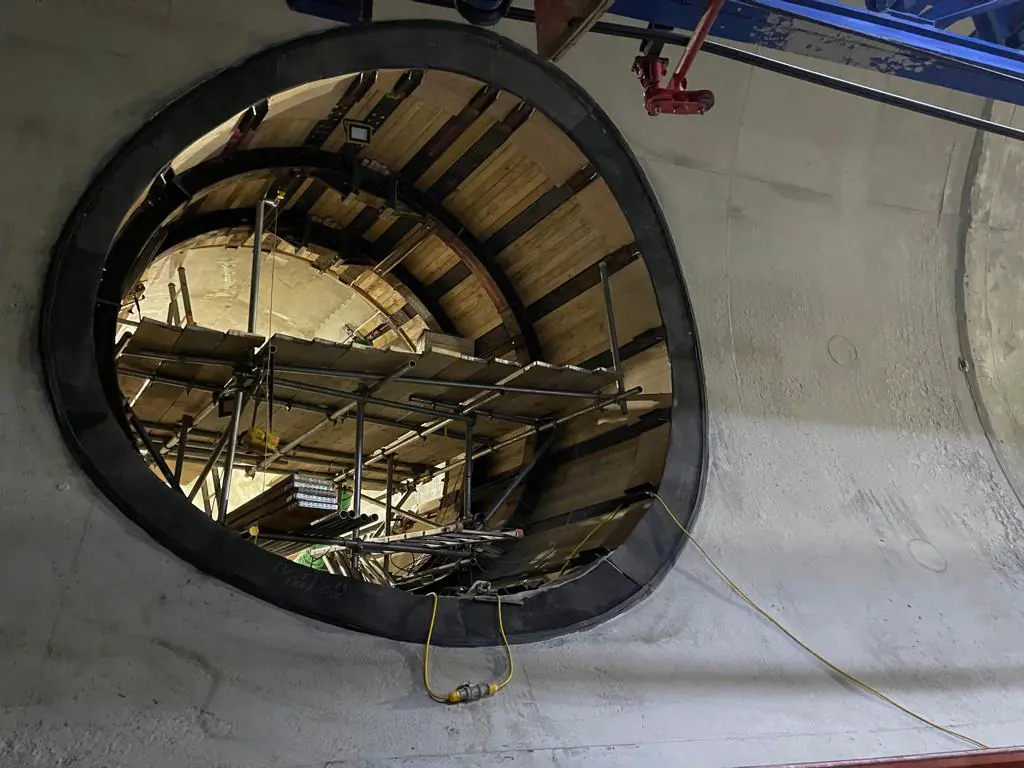 Interior of a tunnel under construction showing scaffolding and wooden supports inside an oval-shaped concrete opening.