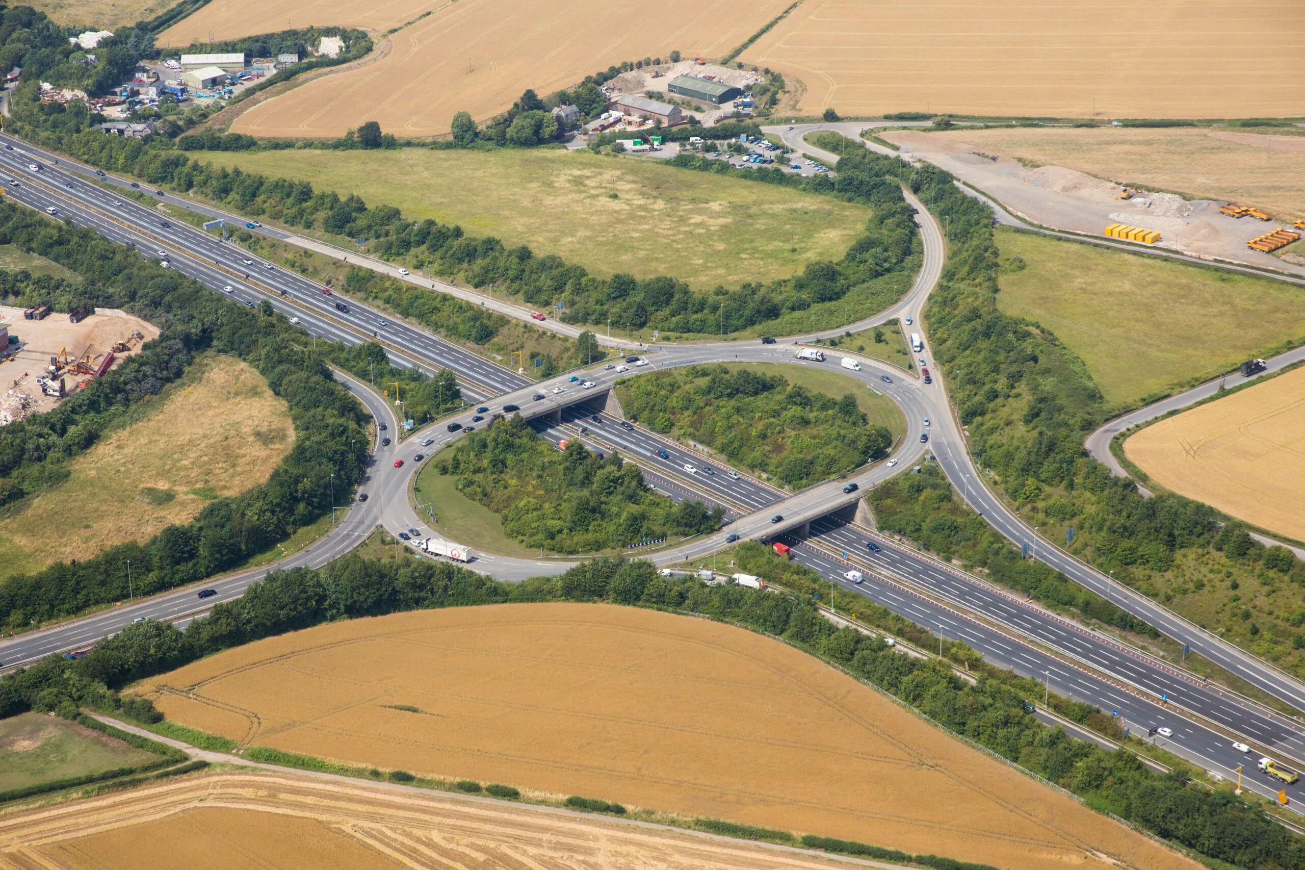 Aerial view of a highway interchange surrounded by green fields and trees, showing multiple lanes and smooth traffic flow.