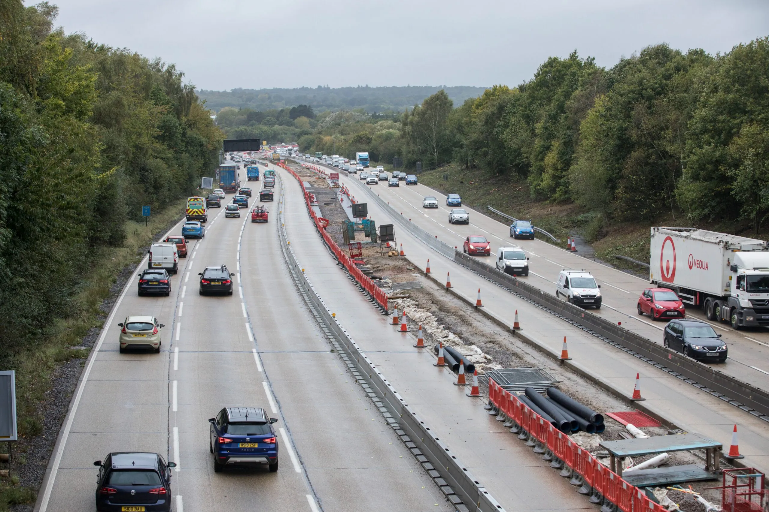 Highway construction zone with traffic cones and barriers guiding vehicles through active work area.