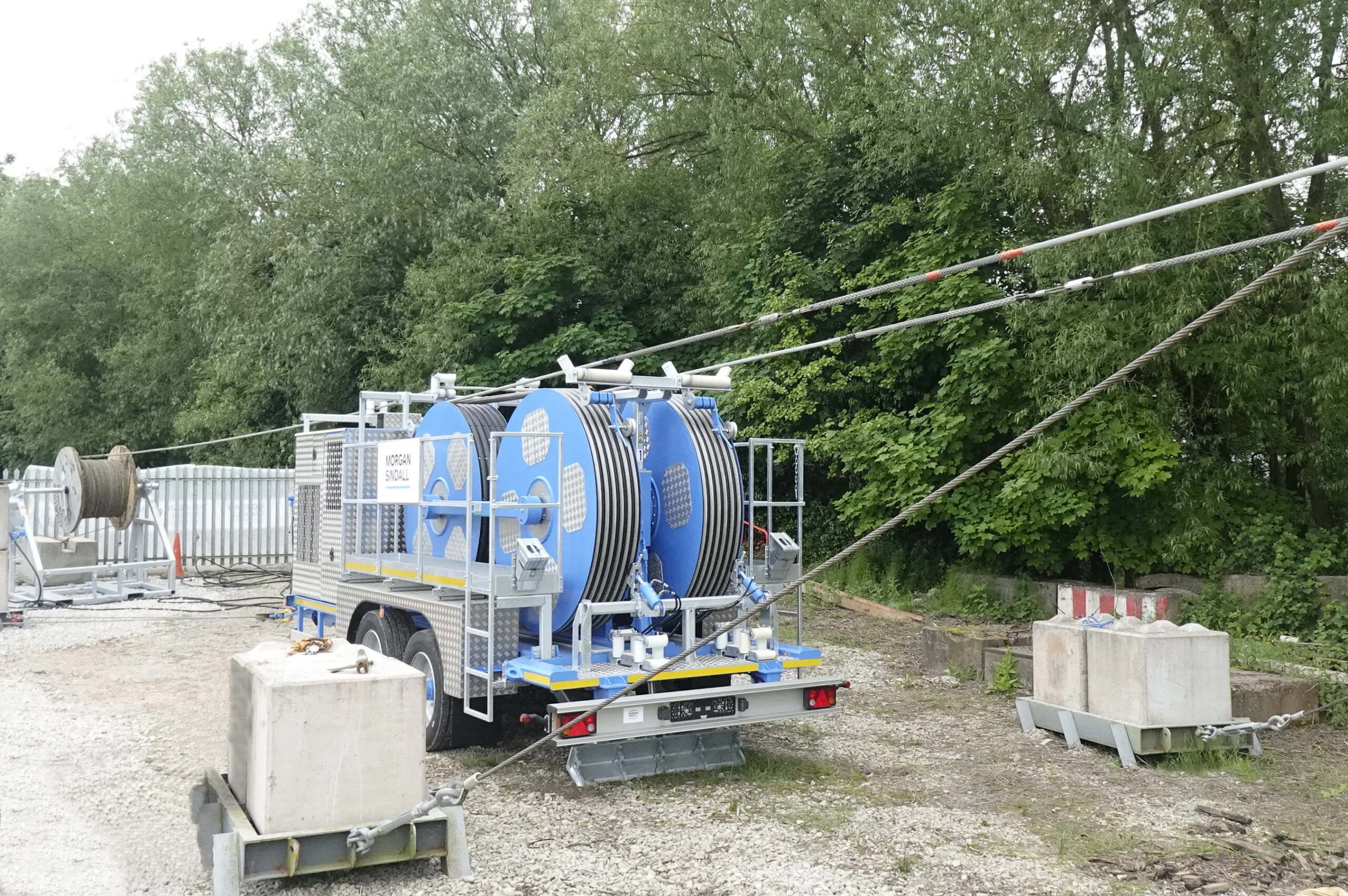 Large cable drum mounted on a trailer at a construction site, with visible power lines and safety barriers.