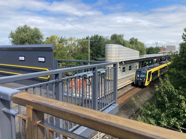 Bridge construction scene with a view of industrial buildings and landscape below, taken from the bridge deck.