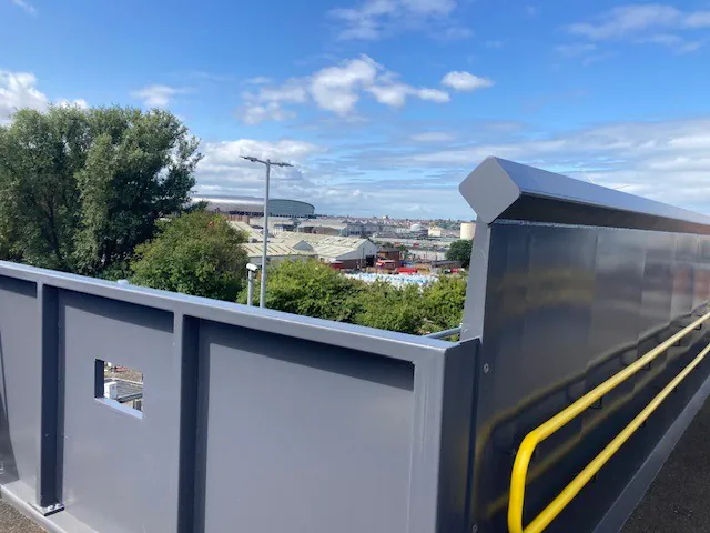 View from a newly constructed bridge railing overlooking industrial buildings under a partly cloudy sky.