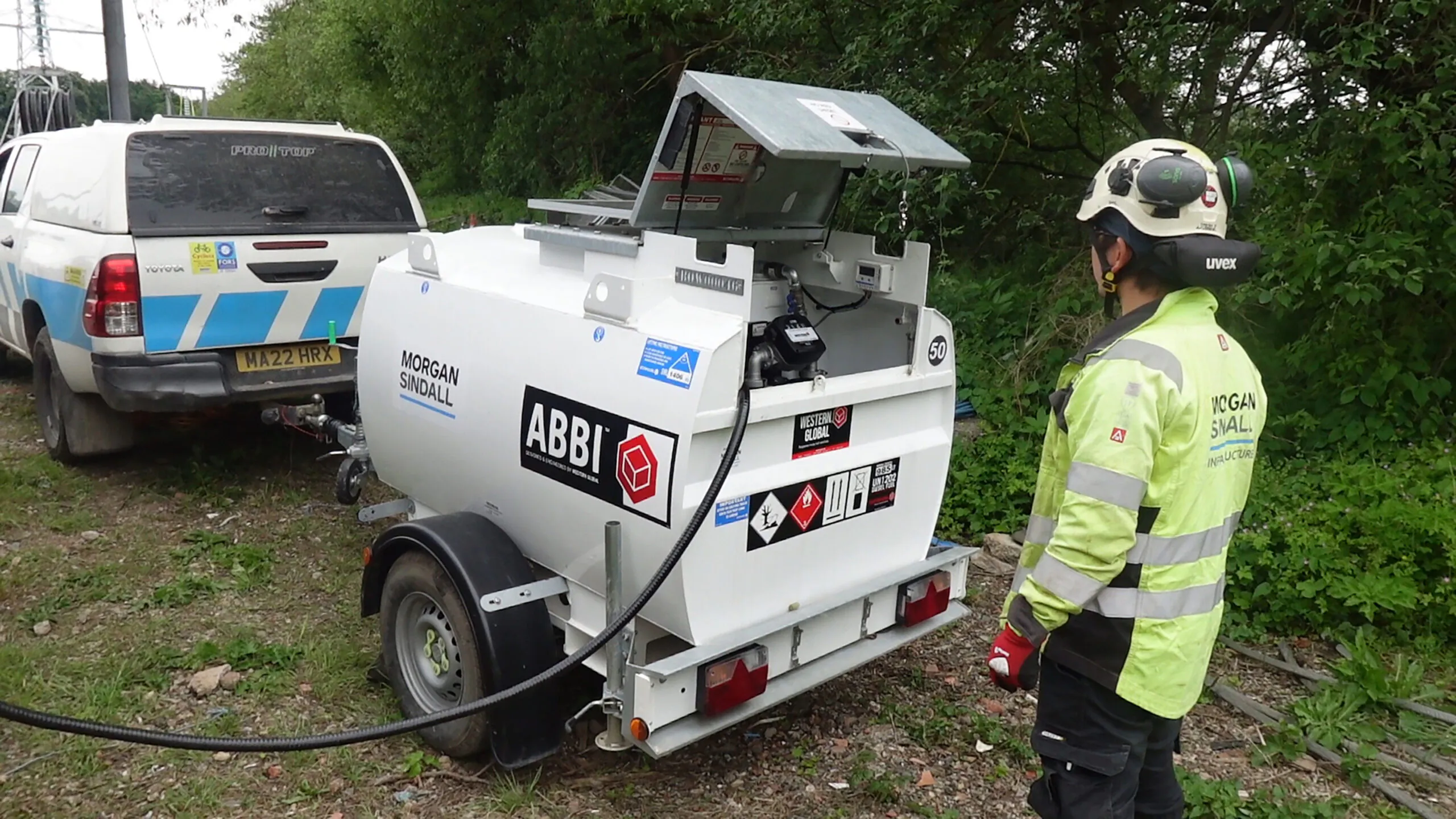 Solar-powered fuel bowser trailer branded "Morgan Sindall" parked at a construction site with other equipment nearby.