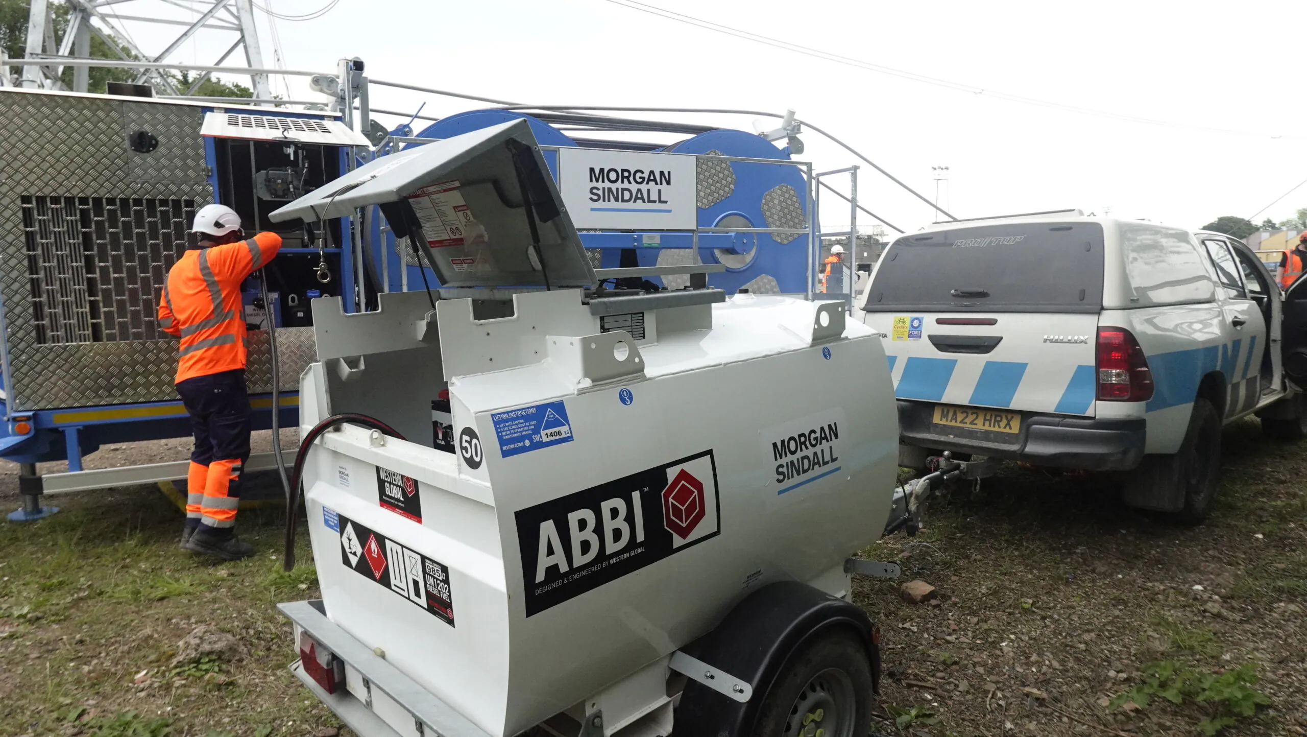 ABBI solar-powered fuel bowser trailer branded "Morgan Sindall," operated by two workers at an outdoor site with other equipment nearby.
