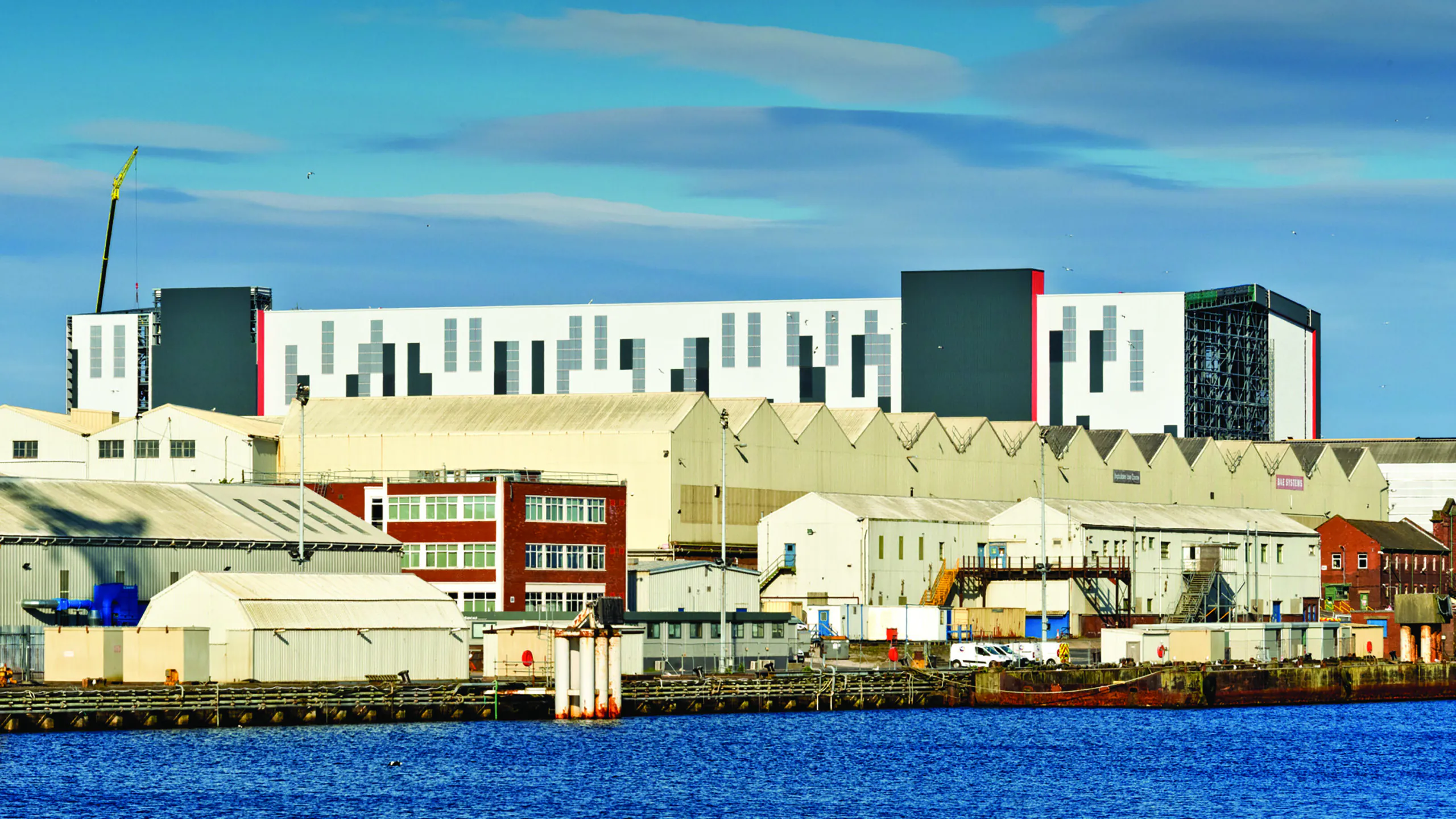 Large industrial complex near water with multiple warehouses and modern geometric building designs under clear skies.