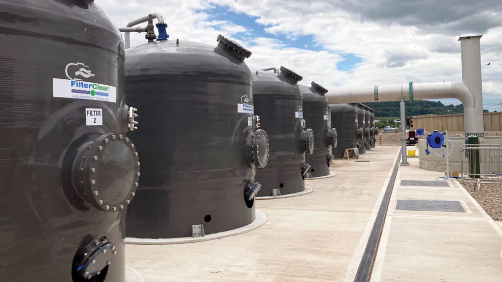 Row of large black cylindrical tanks labeled "FilterClear" at an industrial facility under a partly cloudy sky.