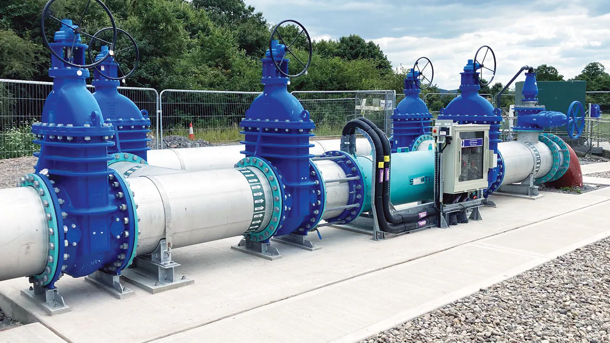 Series of blue valves connected to industrial pipes under partly cloudy skies.
