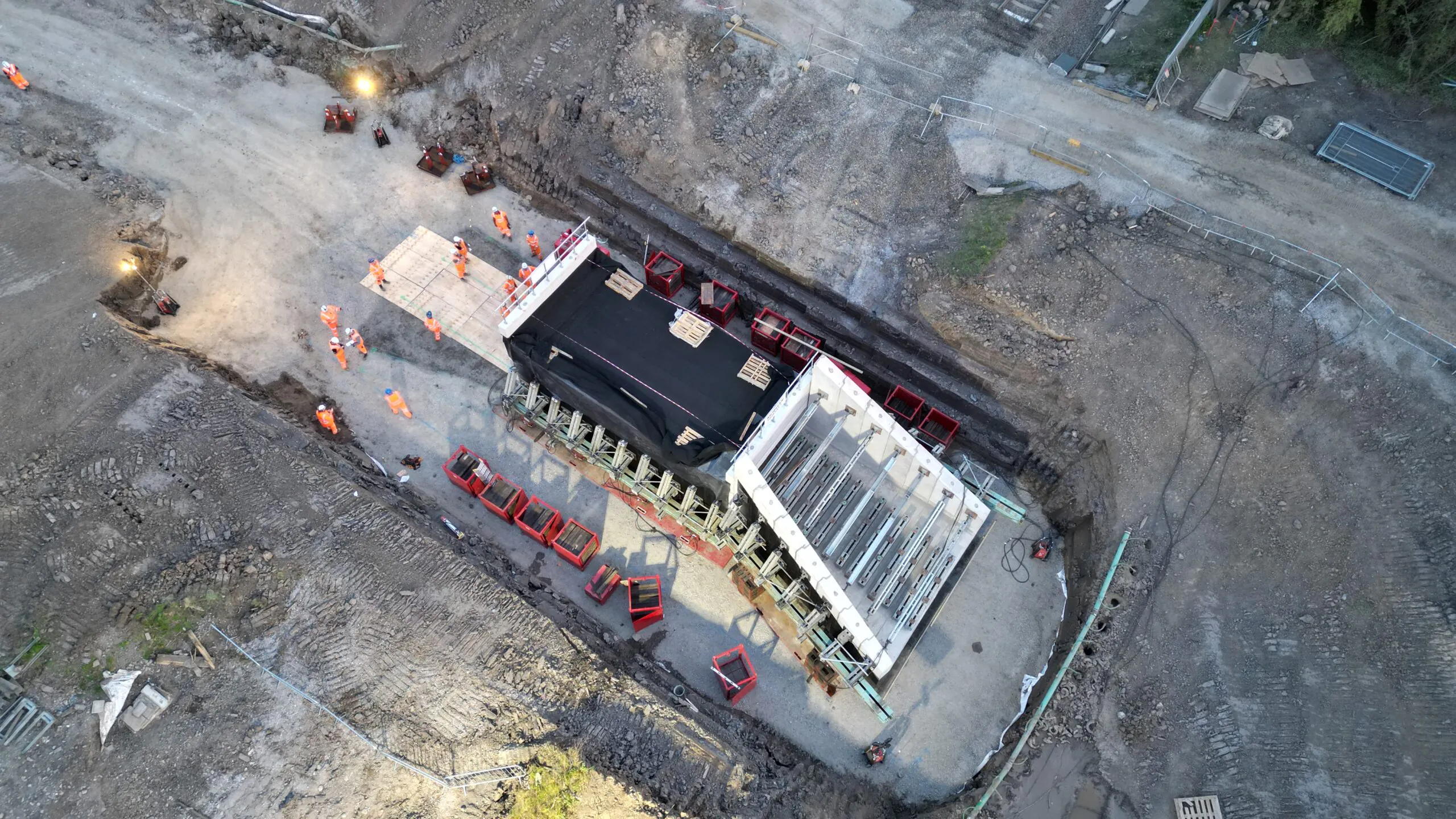 Aerial view of a construction site with a large structure being built; workers in high-visibility clothing and construction equipment are visible.