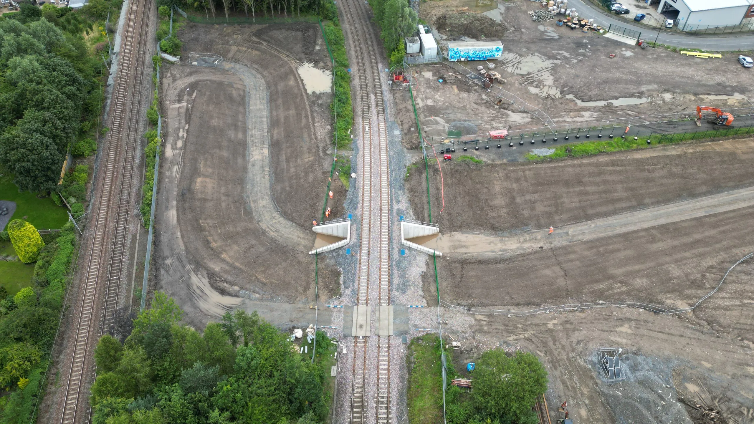 Aerial view of railway tracks intersecting with newly constructed pathways; construction machinery and materials are visible in the surrounding area.