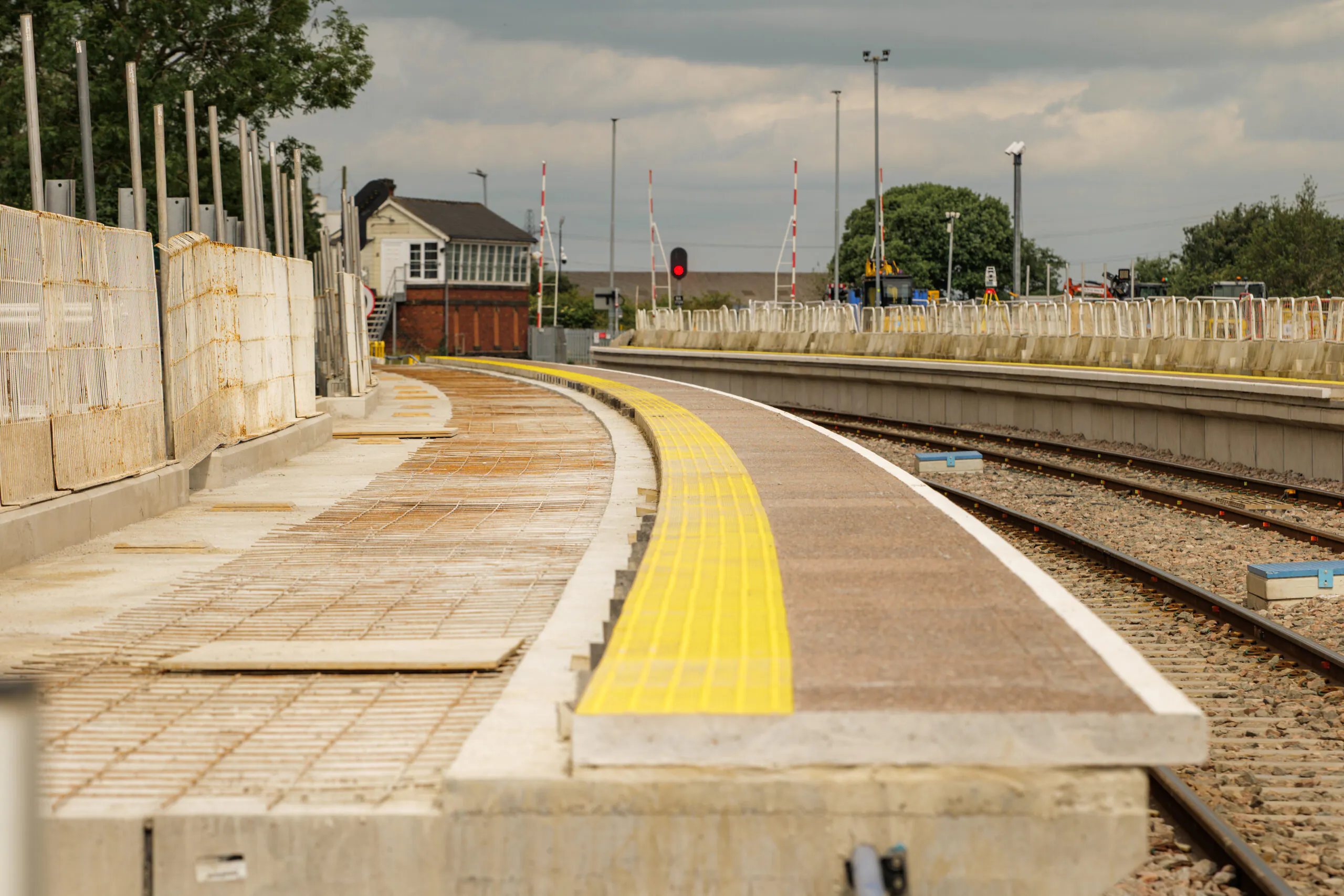 Newly constructed curved concrete platforms alongside dual rail lines leading toward signaling equipment and a small brick control tower.