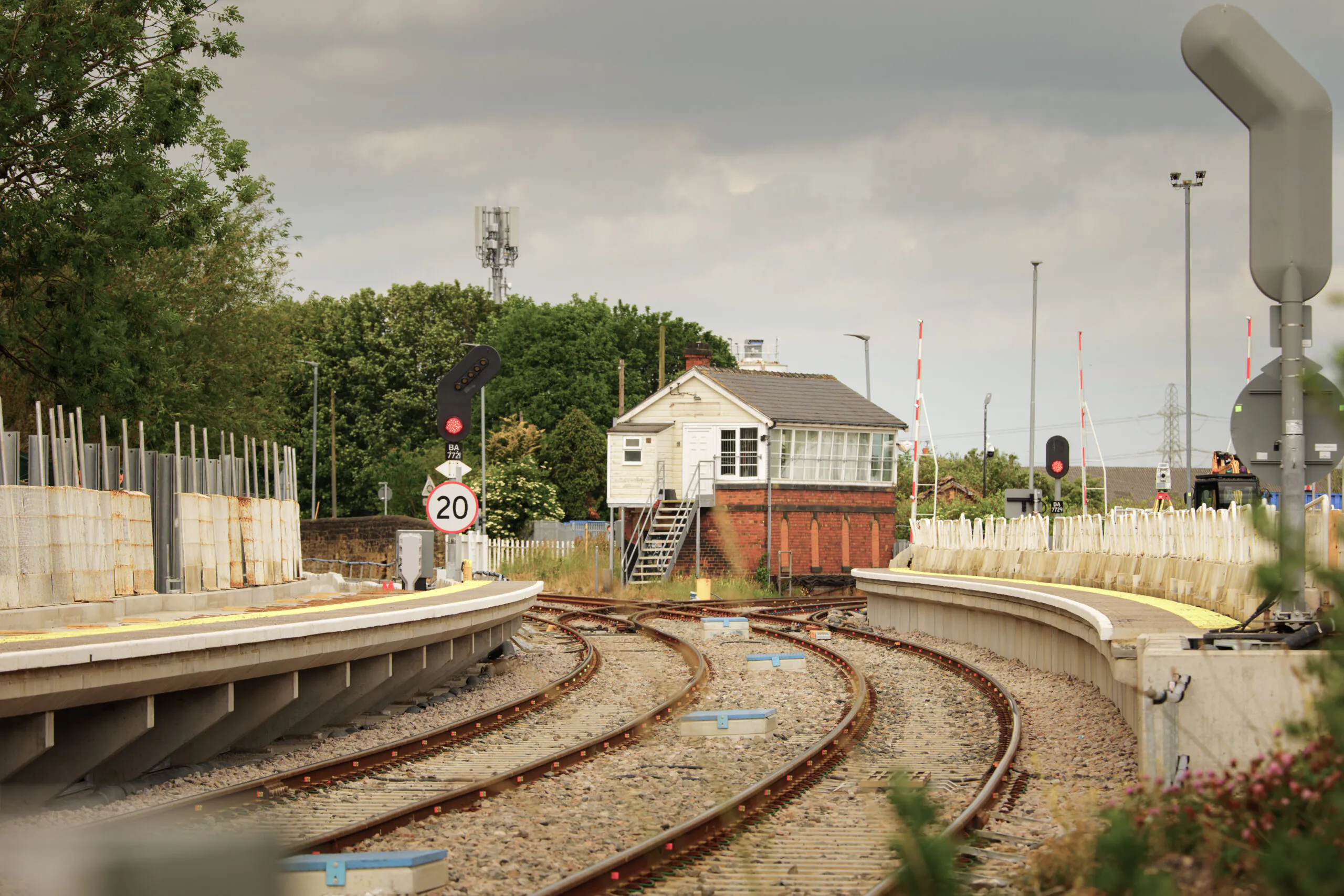 Railway tracks leading to an old signal box building surrounded by construction work for new platforms and signals.