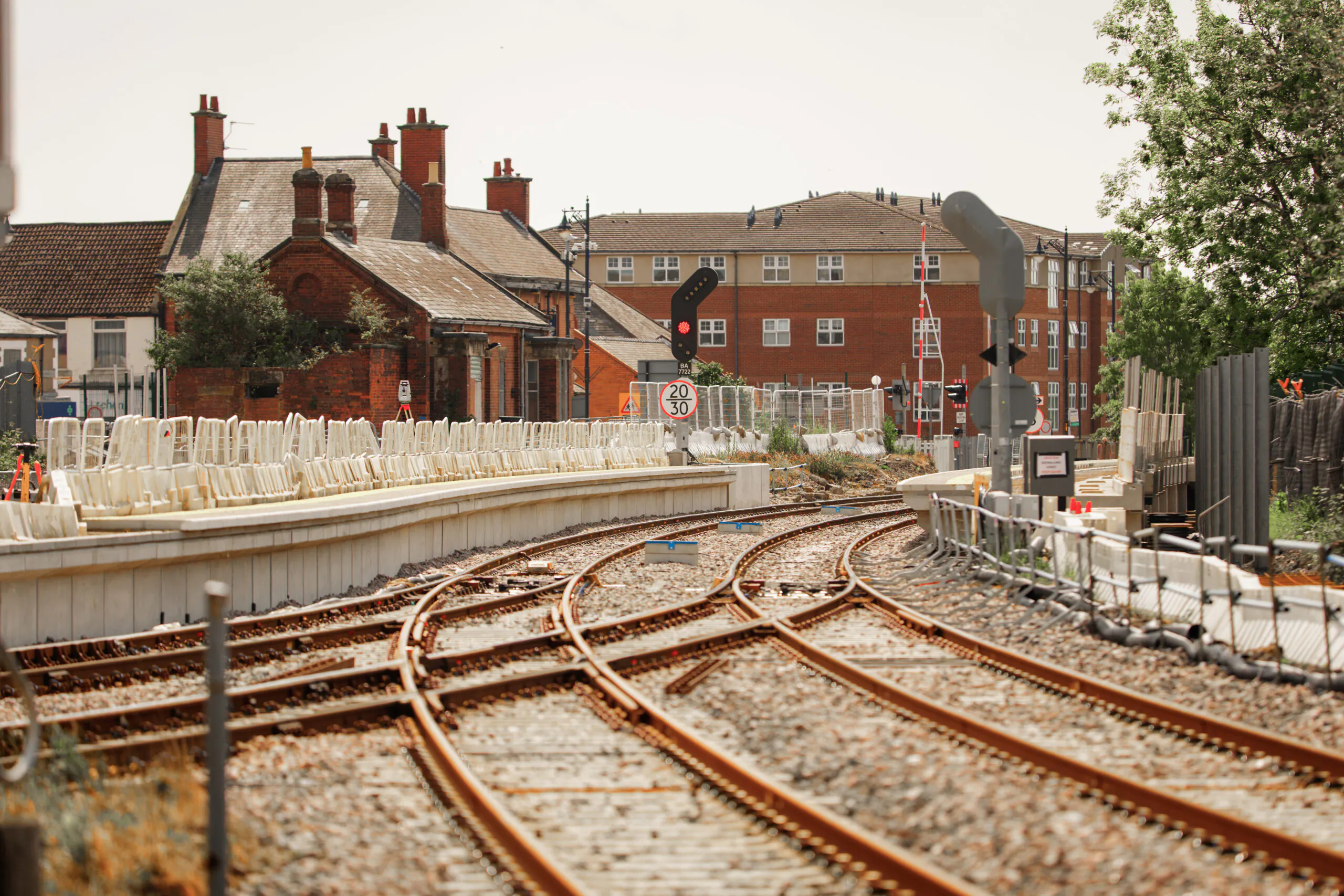 Multiple rail lines converging toward signaling equipment and a small brick control tower; surrounding residential buildings undergoing renovation.