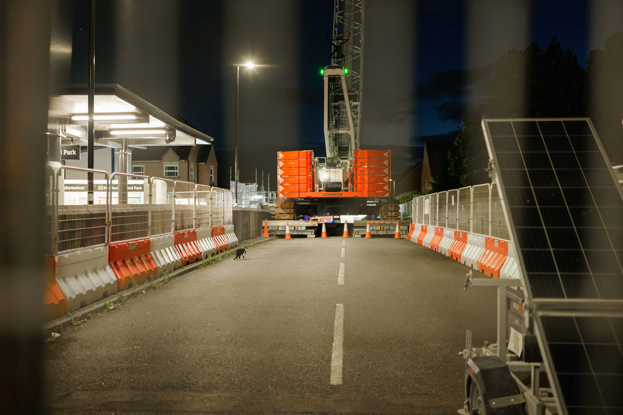 Rear view of heavy machinery on an empty road at night, surrounded by safety barriers.