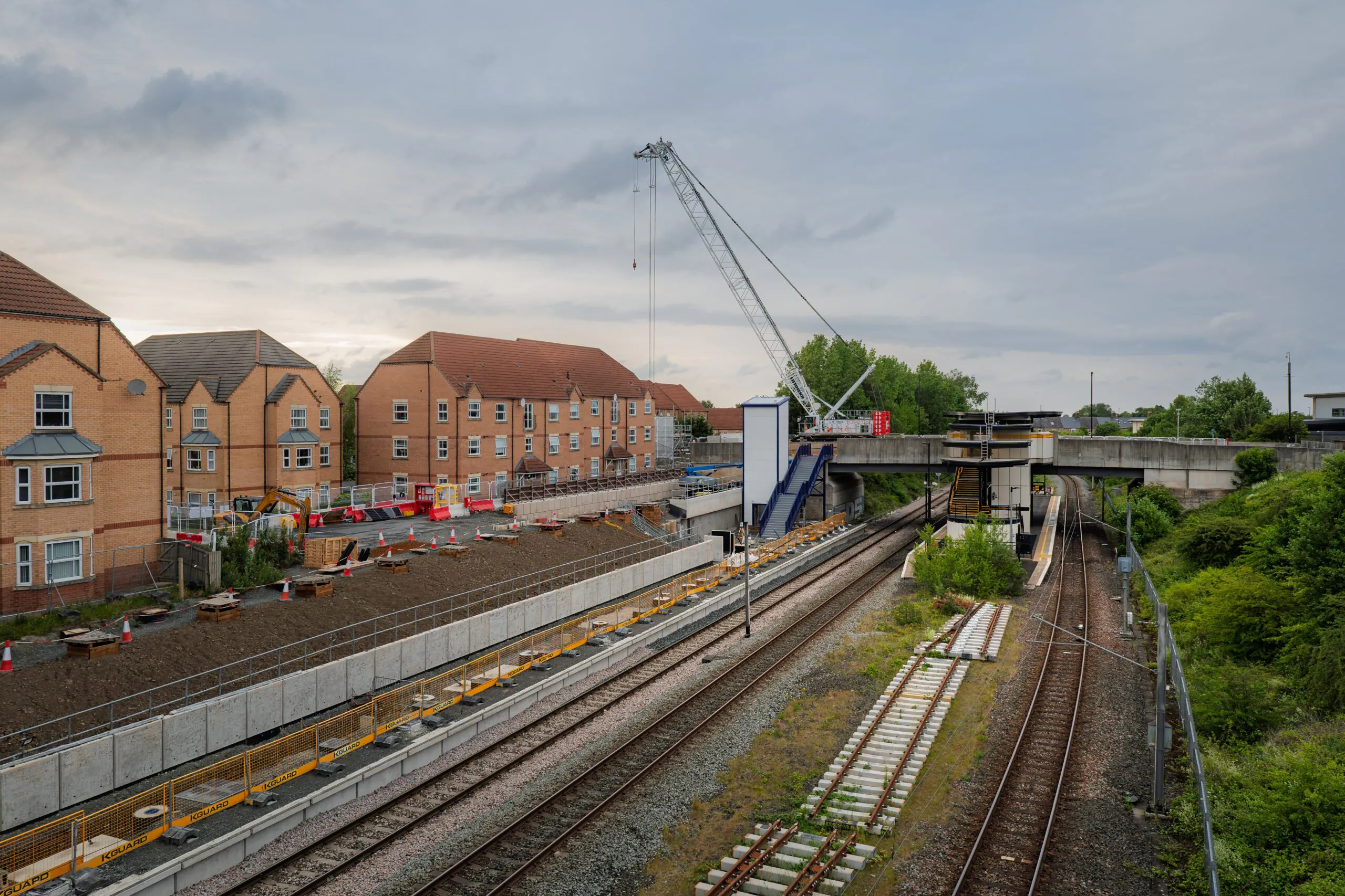 Nighttime construction scene with workers unloading large prefabricated building sections from trucks using heavy machinery, surrounded by scaffolding.