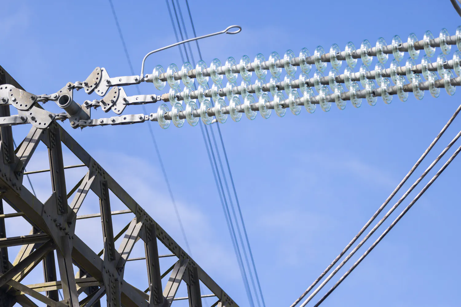 Close-up of a transmission tower section showing insulators and connectors, with a clear blue sky in the background.