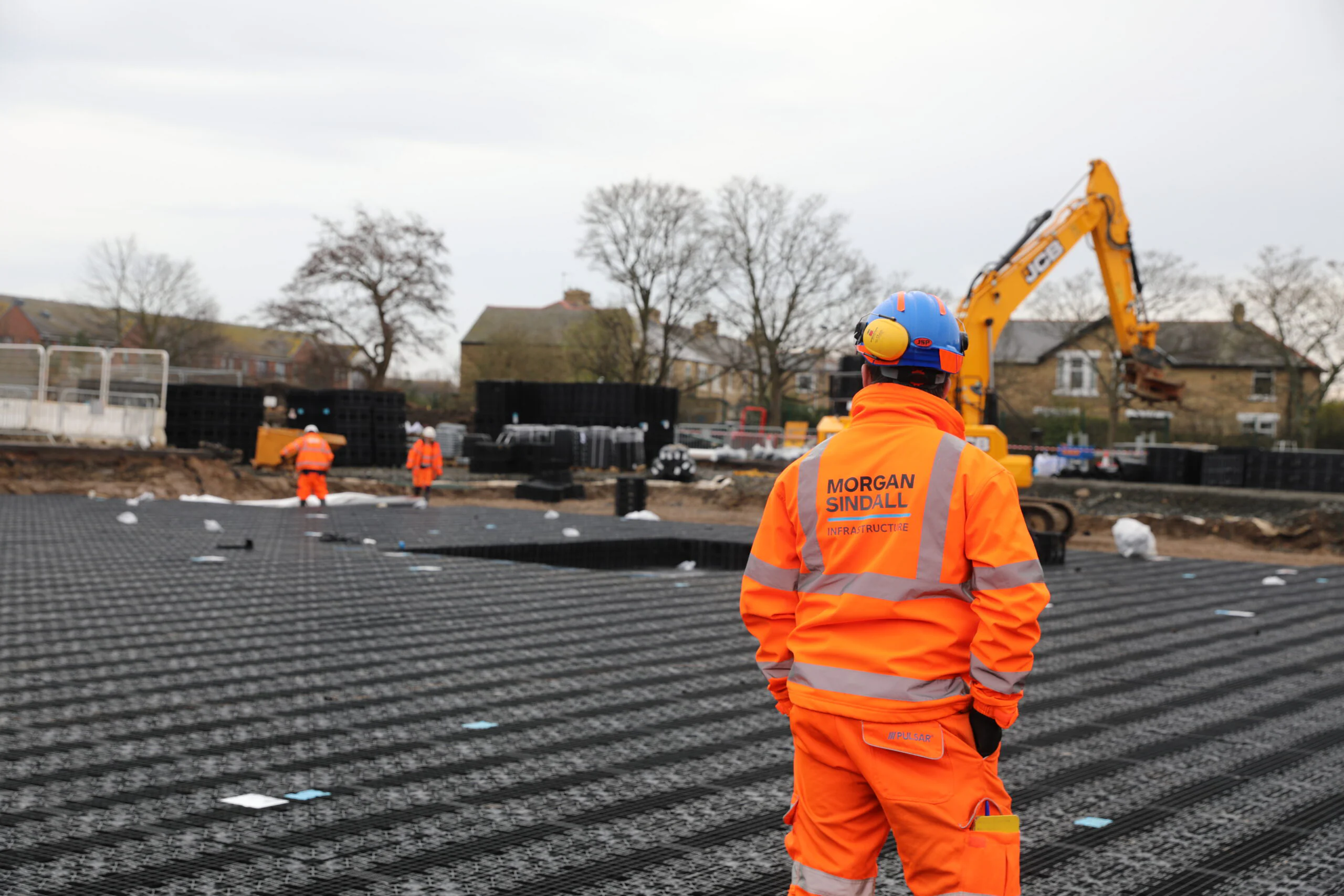 Excavator digging beside railway tracks during infrastructure work, with workers in safety gear and temporary fencing.