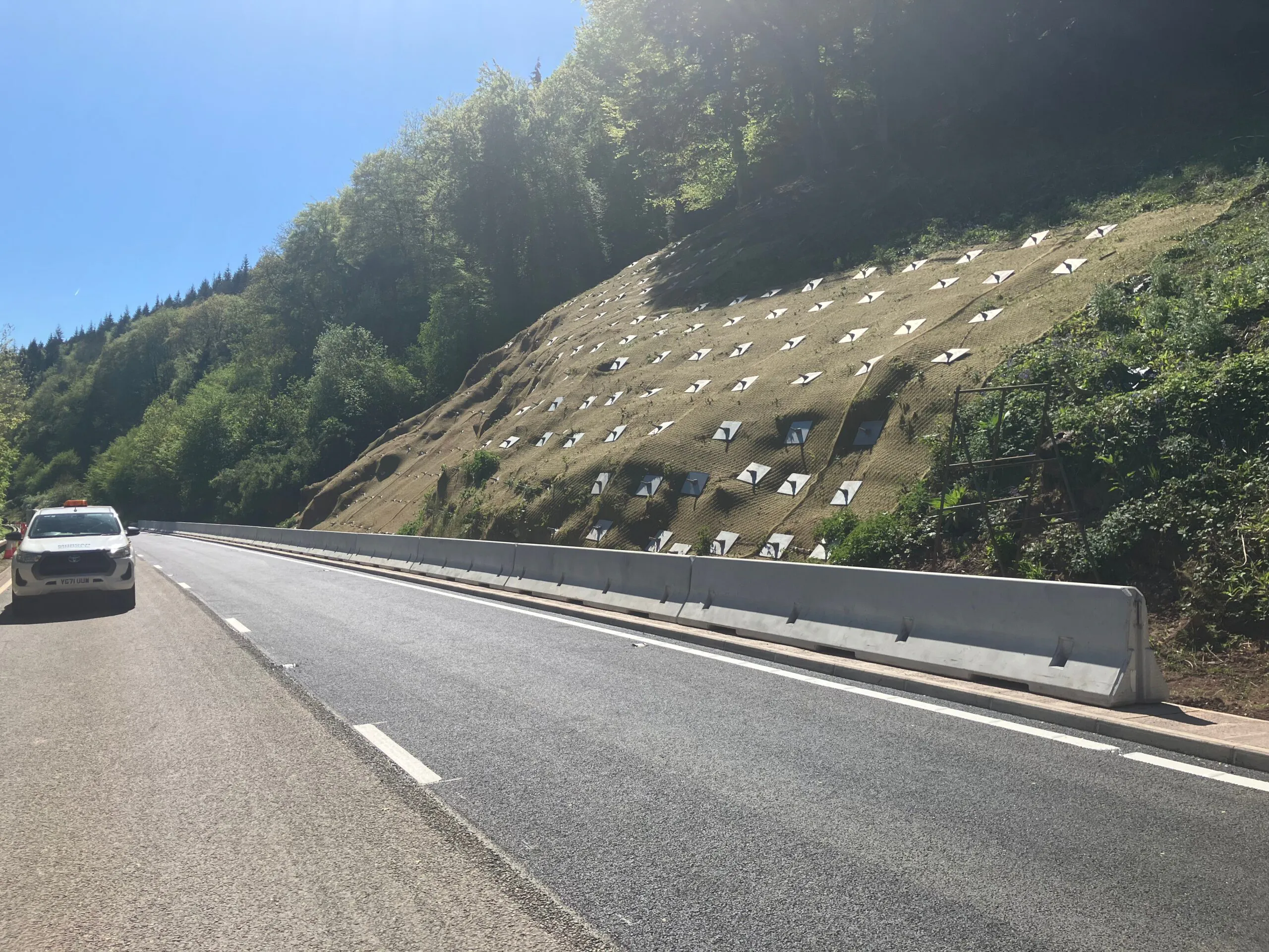 Completed stabilised slope alongside the A40 at Leys Bend, protected with erosion control matting and soil nail head plates following rockfall remediation works.