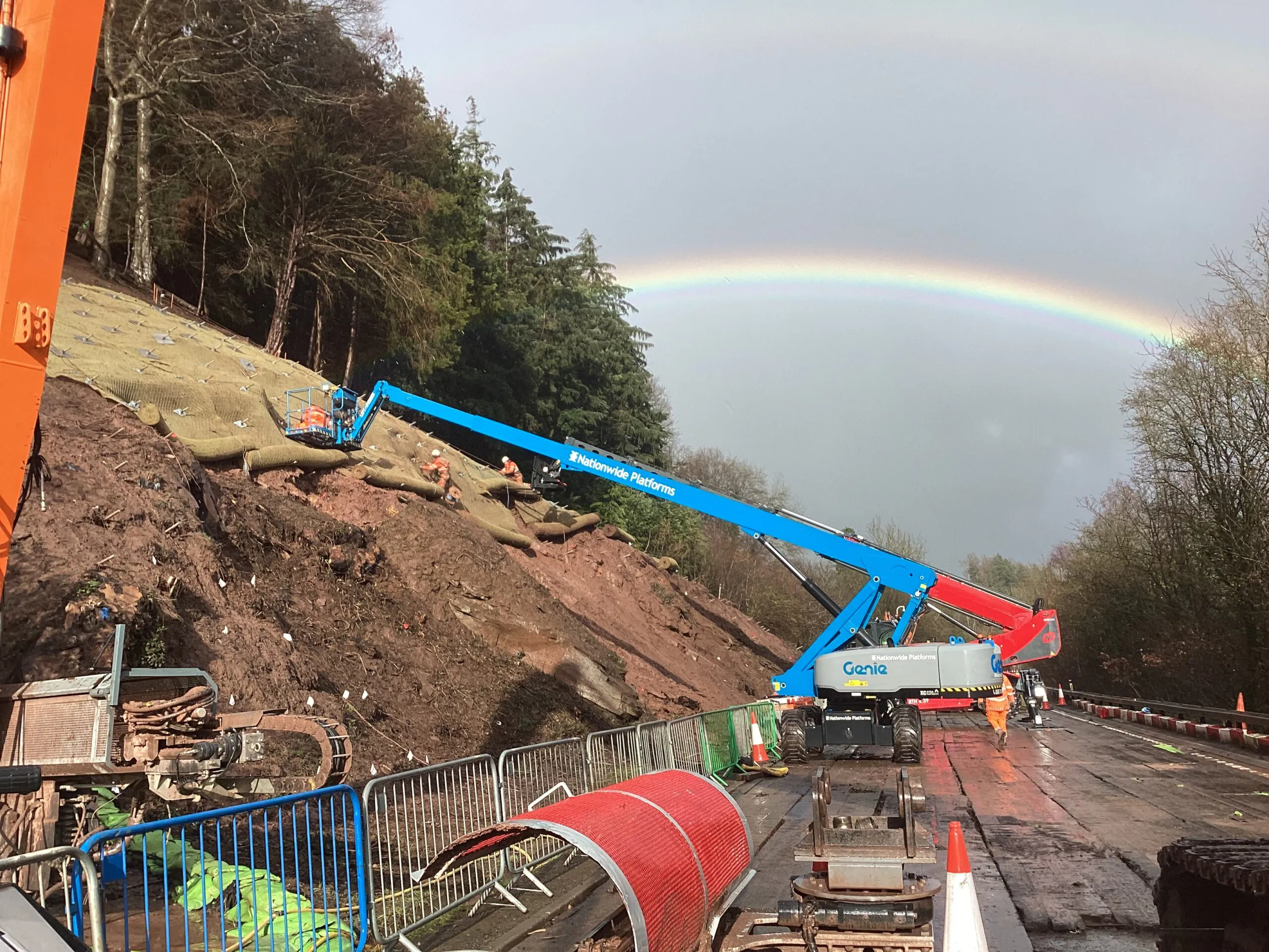 Rockfall stabilisation works in progress at A40 Leys Bend, with access equipment and construction teams working on the slope beside the carriageway.