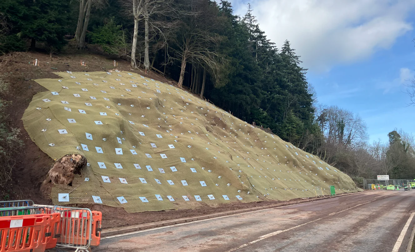Roadside view of the stabilised slope at A40 Leys Bend following installation of soil nails, mesh and erosion control measures.